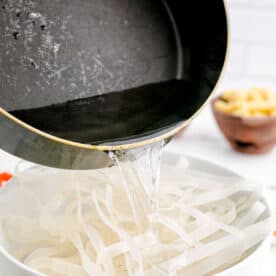 boiling water is being poured onto rice noodles in a white bowl