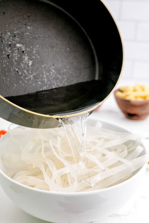 boiling water is being poured onto rice noodles in a white bowl
