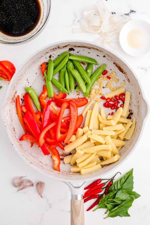 snow peas, red bell peppers, garlic, thai chilies, and corn is added to a nonstick skillet