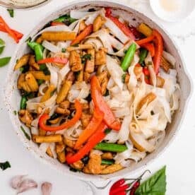 rice noodles and chicken are added to a nonstick skillet along with other vegetables and sauce