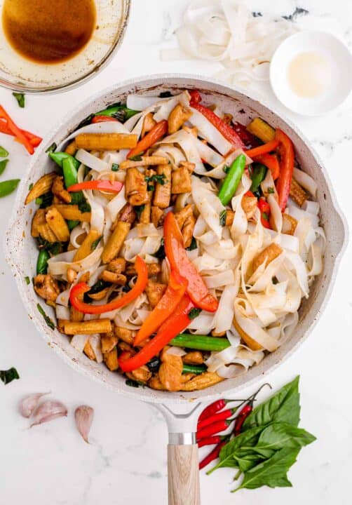 rice noodles and chicken are added to a nonstick skillet along with other vegetables and sauce