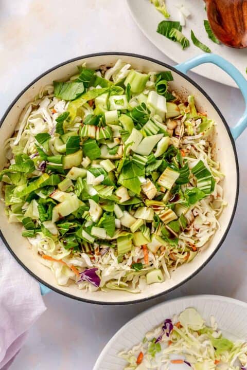 bok choy and cabbage mixture added in an enameled cast iron skillet