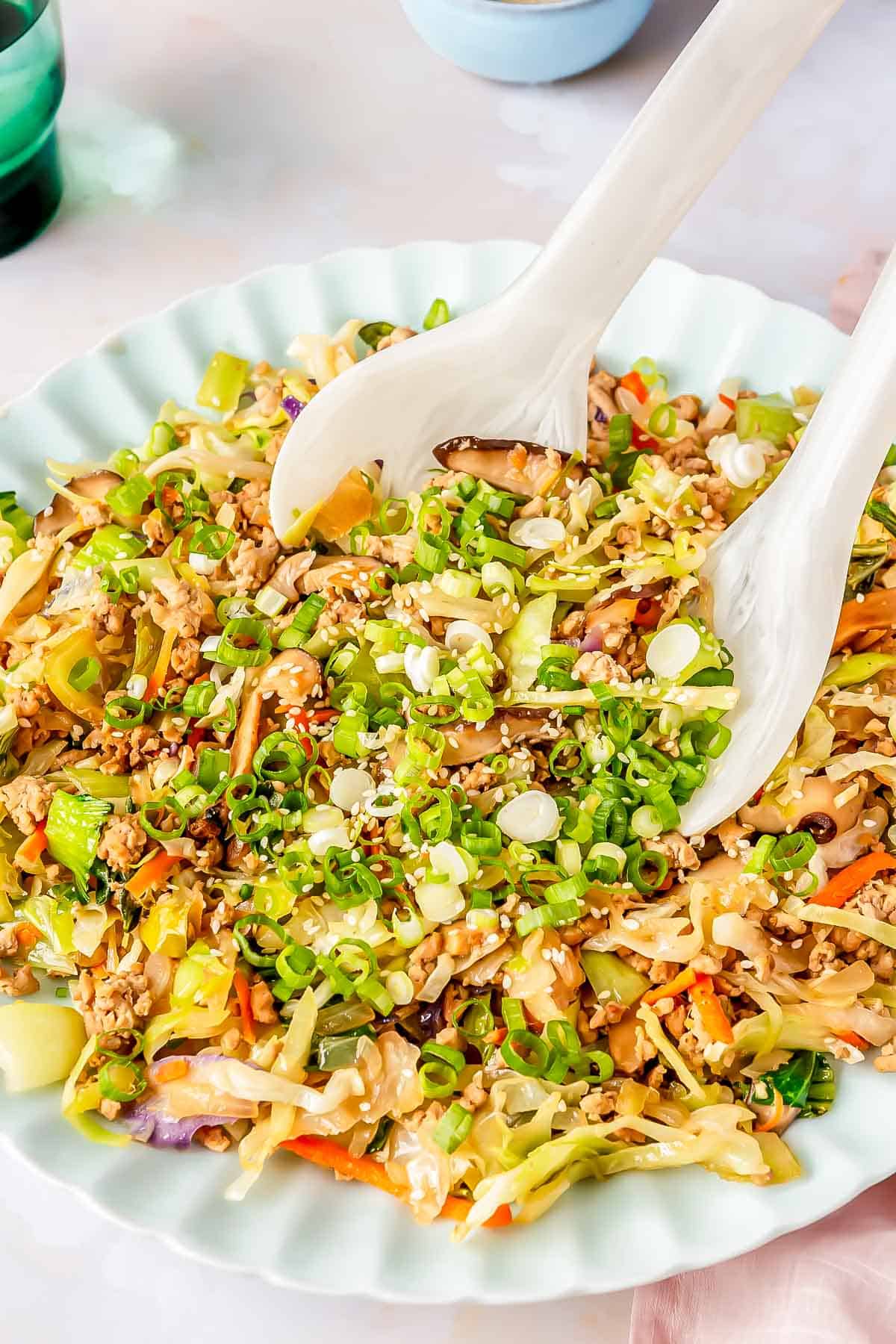 eggroll filling on a scalloped plate with 2 white melamine spoons scooping out the filling