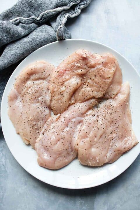 raw thin cut chicken breasts seasoned with salt and pepper on a white plate
