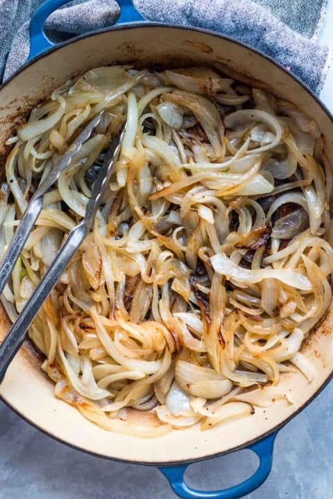 onions being caramelized in a dutch oven with metal tongs in the pot