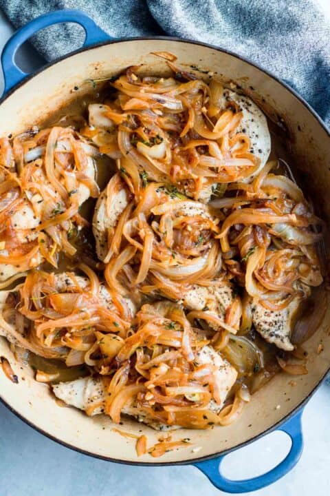 chicken is added back into the dutch oven and caramelized onions are topped on the chicken