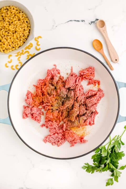 ground beef and seasonings in a cast iron skillet next to fresh parsley and dried pasta