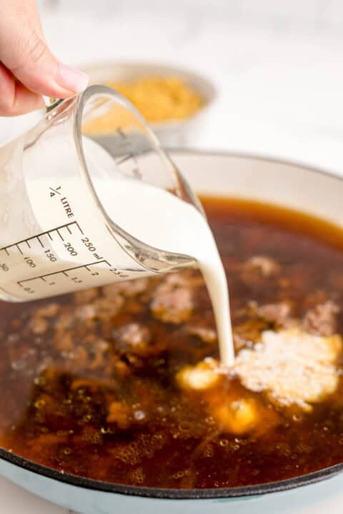 cream is being poured into a cast iron skillet with other liquids