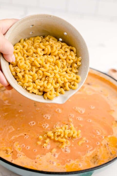 dried macaroni pasta is being added to a cast iron skillet