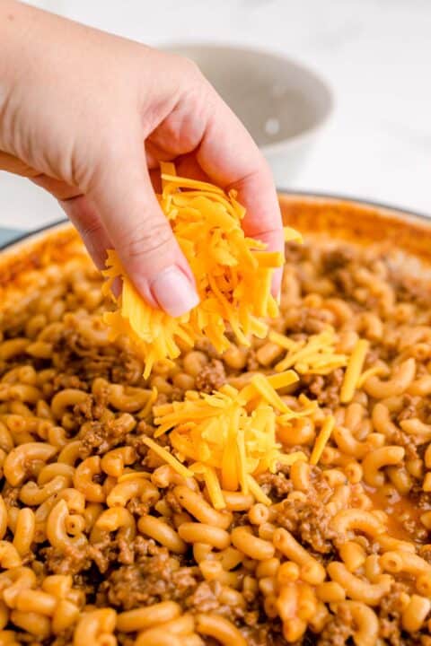 freshly grated cheddar cheese is being sprinkled on top of cooked beef and macaroni pasta