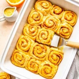 orange rolls baked and glazed in a white baking dish with a metal spatula holding one
