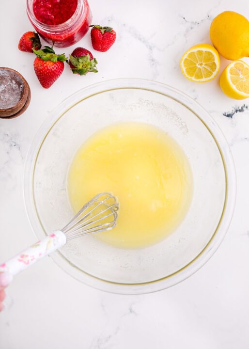 a whisk in a clear bowl whisks together melted butter and sugar