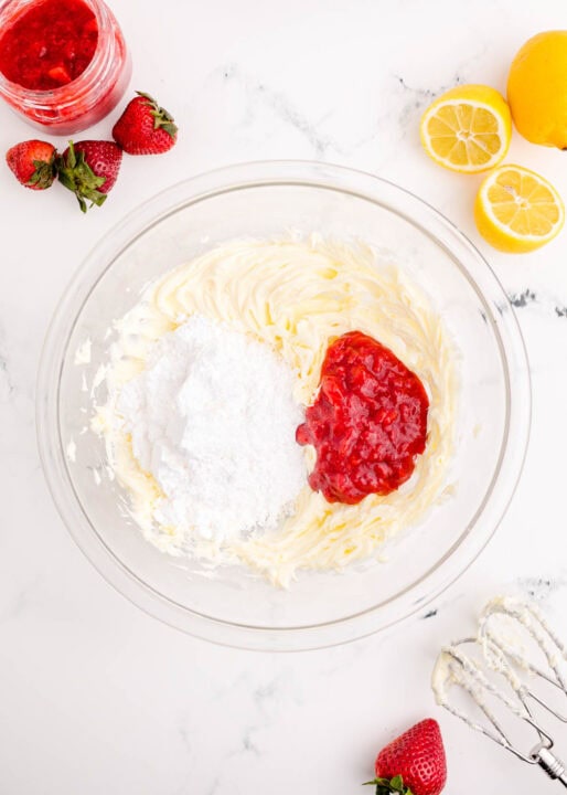 powdered sugar and strawberry jam added to beaten butter in a clear bowl