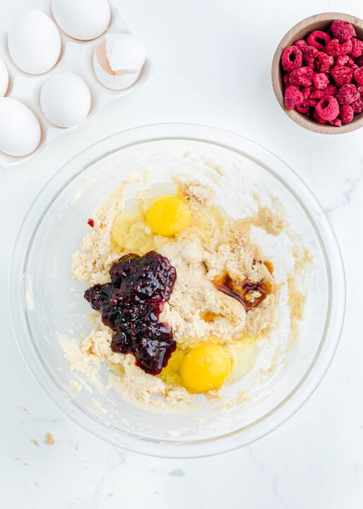 two eggs, raspberry jam, vanilla, and creamed butter and sugar in a clear bowl