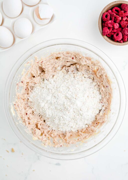 flour and oats added to raspberry cookie dough mix in a clear bowl