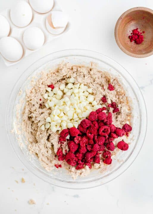 freeze-dried raspberries and white chocolate chips added to cookie dough batter in a clear bowl