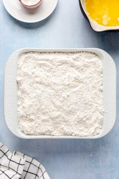 cake mix is poured on top of blueberries in the white square baking dish