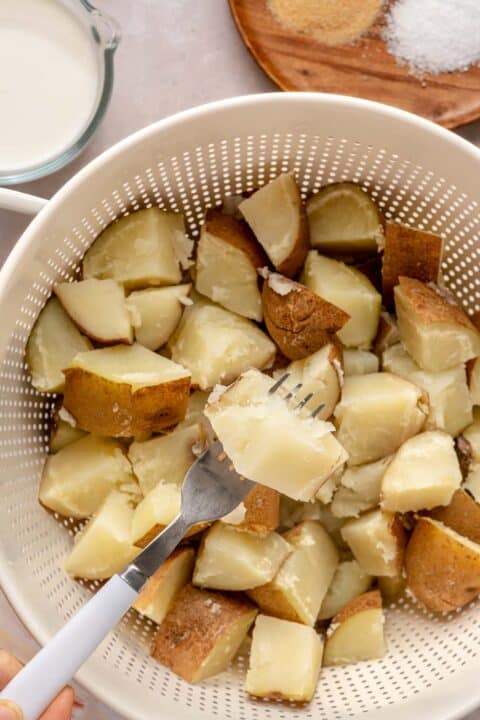 cooked russet potatoes in a colander with a fork piercing one potato wedge