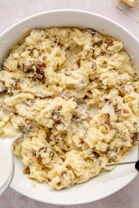 milk is being poured into the bowl of mashed potatoes