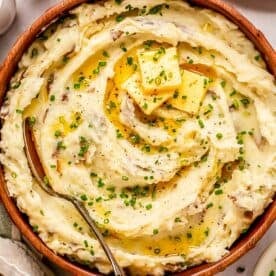 a large bowl of mashed potatoes topped with 3 pads of butter and fresh chives