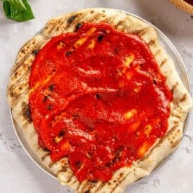 pizza sauce spread on top of grilled pizza dough