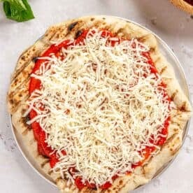shredded mozzarella cheese sprinkled on top of pizza sauce and dough