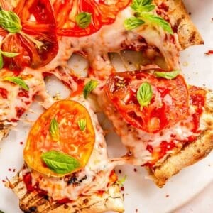 sliced wedges of grilled caprese pizza pulled from the rest of the pizza