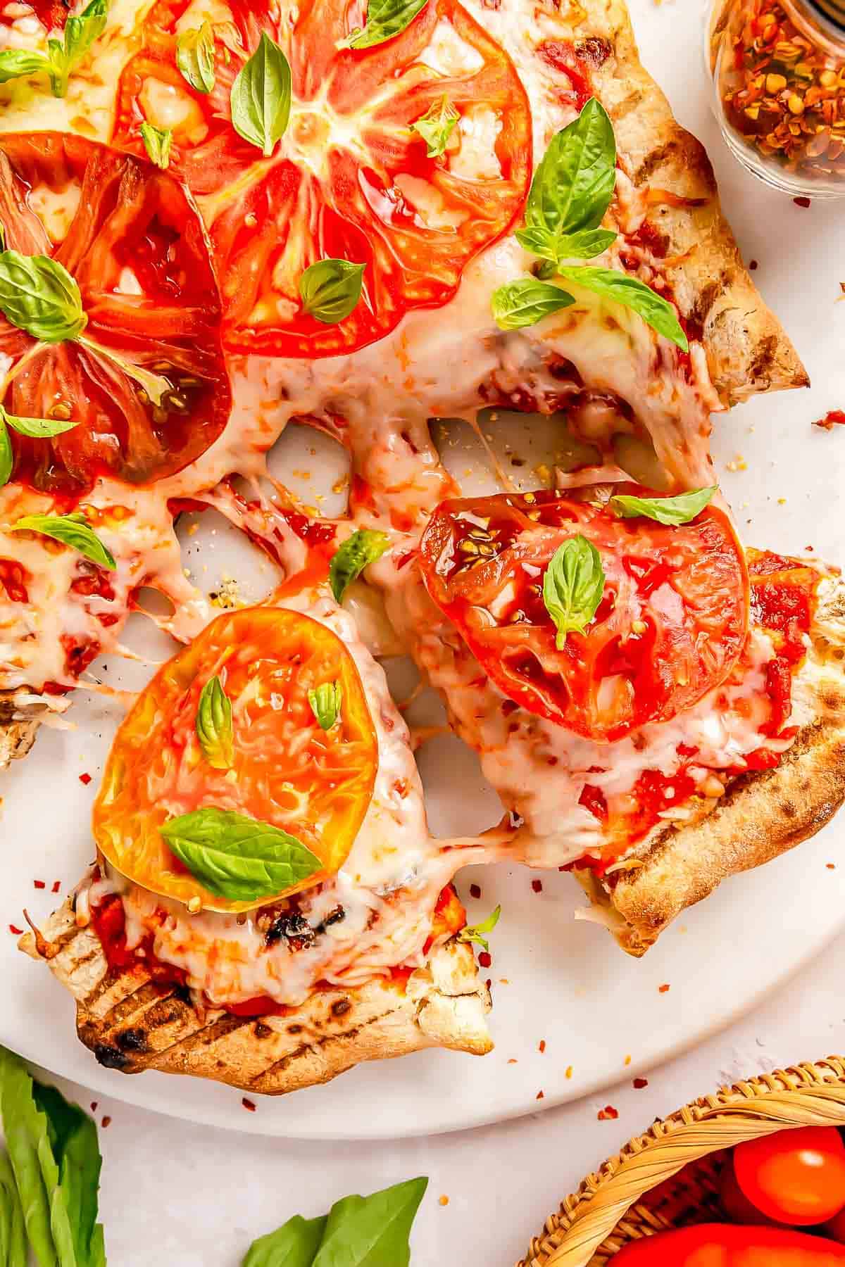 sliced wedges of grilled caprese pizza pulled from the rest of the pizza