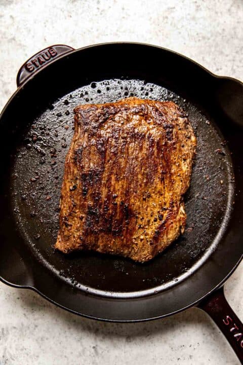 flank steak is browned and seared in a cast iron skillet