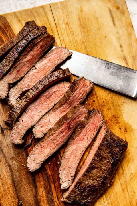 medium temperature flank steak is sliced on a wooden cutting board
