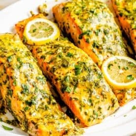 four pieces of honey dijon salmon on a white plate with lemon slices on top