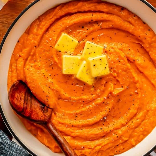 mashed sweet potatoes in a white dutch oven with 5 pads of butter on top with a wooden spoon in the center