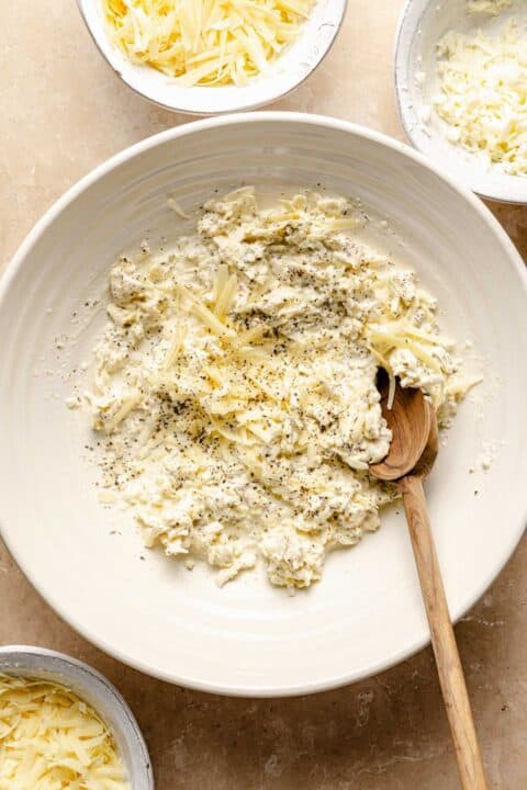 dried basil, heavy cream, and cheeses in a large bowl with a wooden spoon
