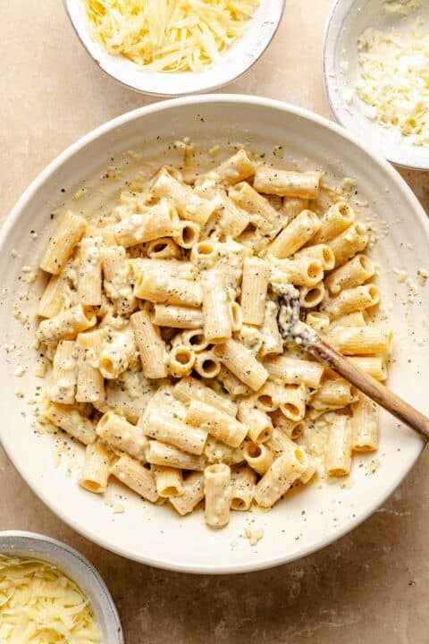 rigatoni pasta tossed in the cheese sauce mixture in a large white bowl with a wooden spoon