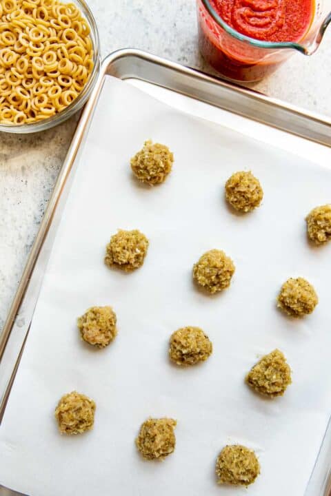 pesto chicken meatballs rolled into small balls and placed onto a parchment paper lined metal baking sheet