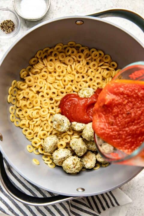 marinara sauce is being poured on top of spaghetti O pasta and chicken meatballs