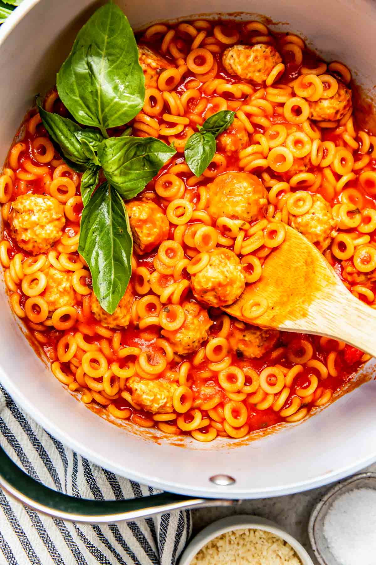 a large pot of spaghetti o's with meatballs in a pot with fresh basil on top and a wooden spoon