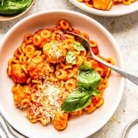 a metal spoon is inserted into the spaghettios in a white bowl with fresh parmesan and basil on top