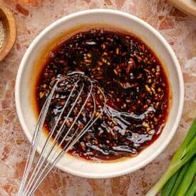 honey garlic sauce being whisked in a white bowl next to fresh green onions
