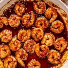 shrimp added to the honey garlic sauce in the white skillet