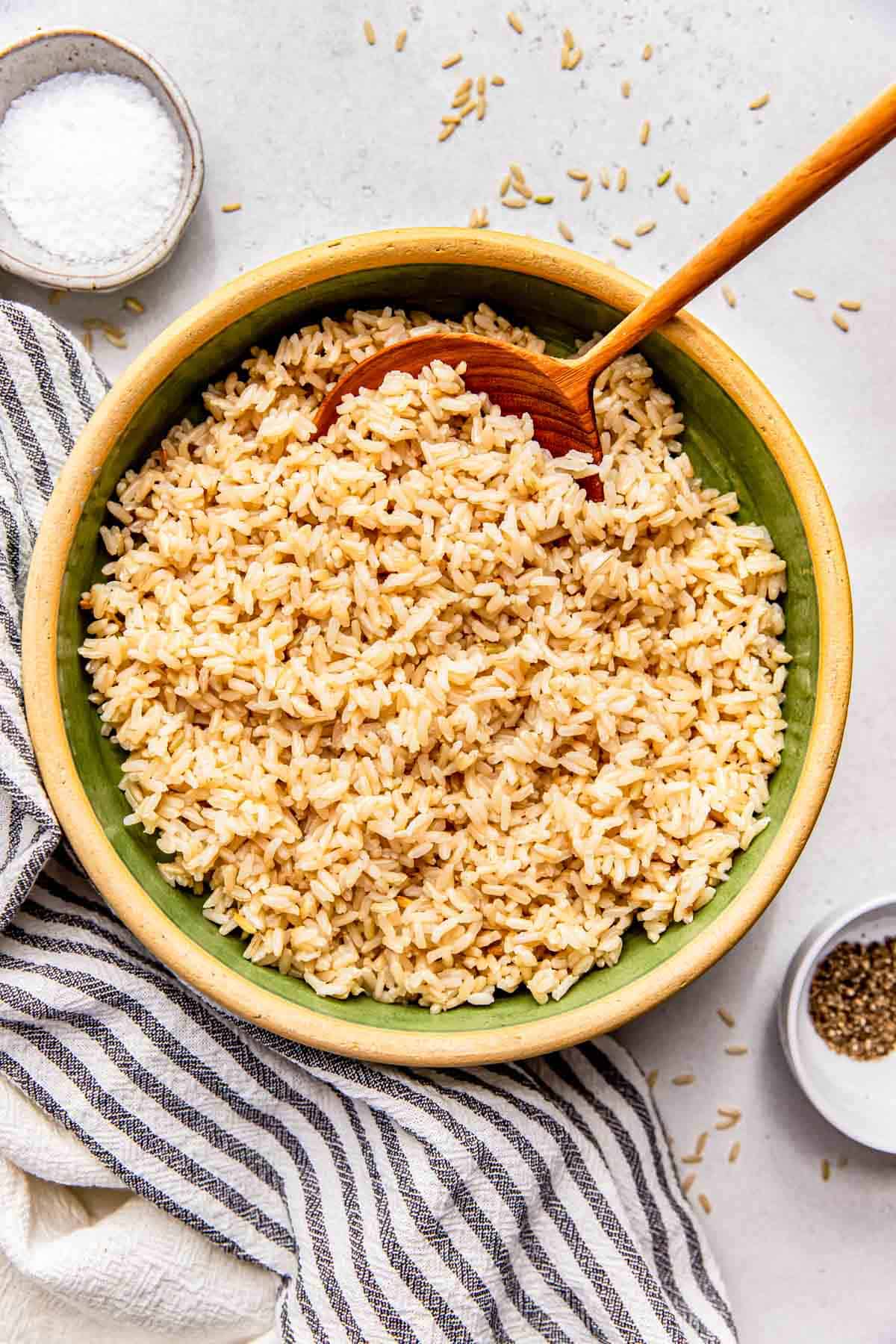a green bowl with a wooden spoon is filled with cooked brown rice