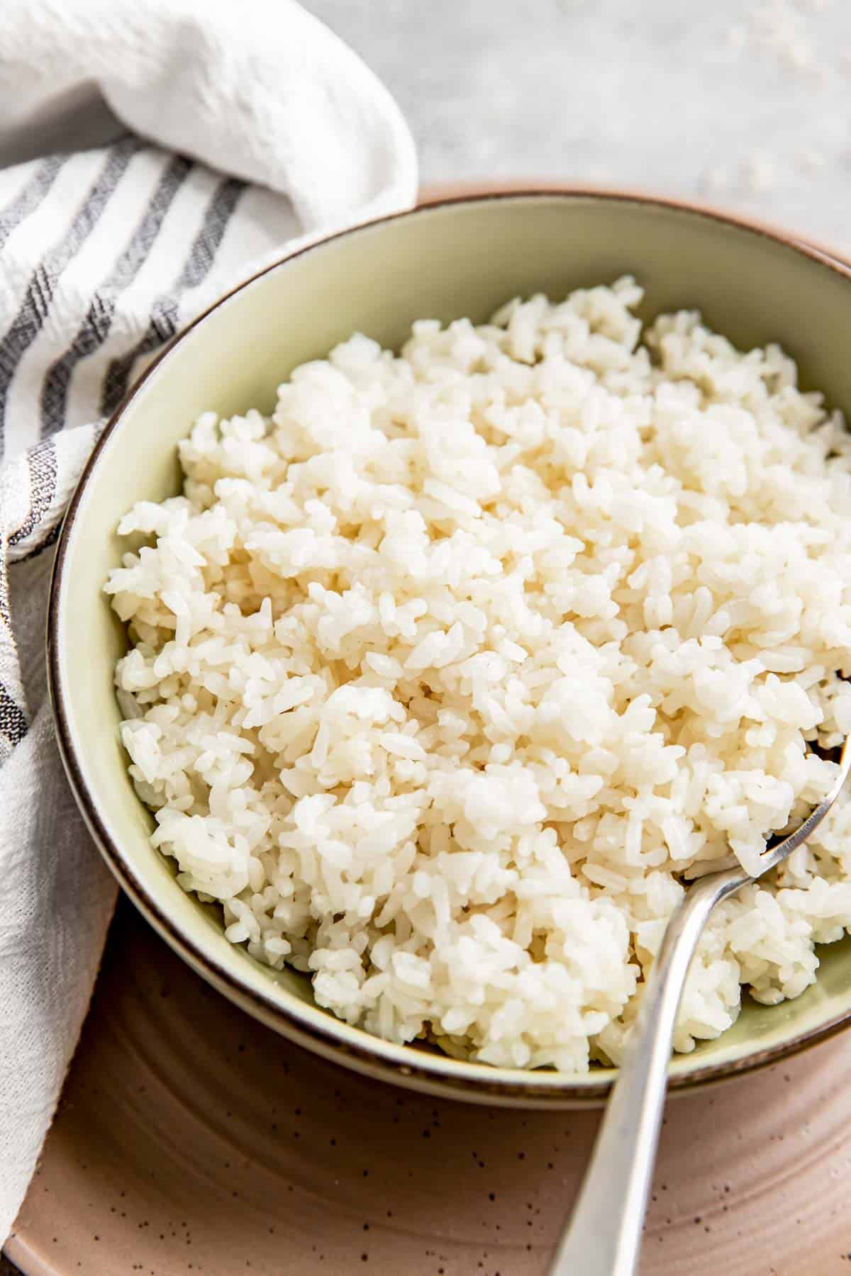 a bowl of cooked white rice is in a green bowl next to a metal spoon