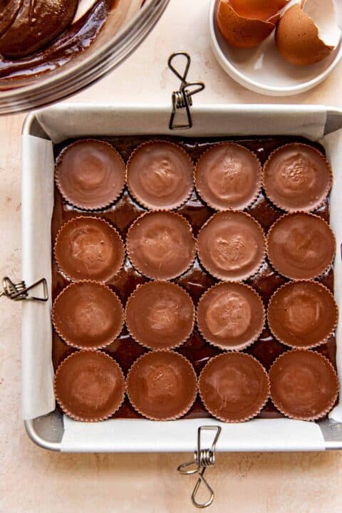 16 reese's cups are added on top of the brownie batter in the square baking pan