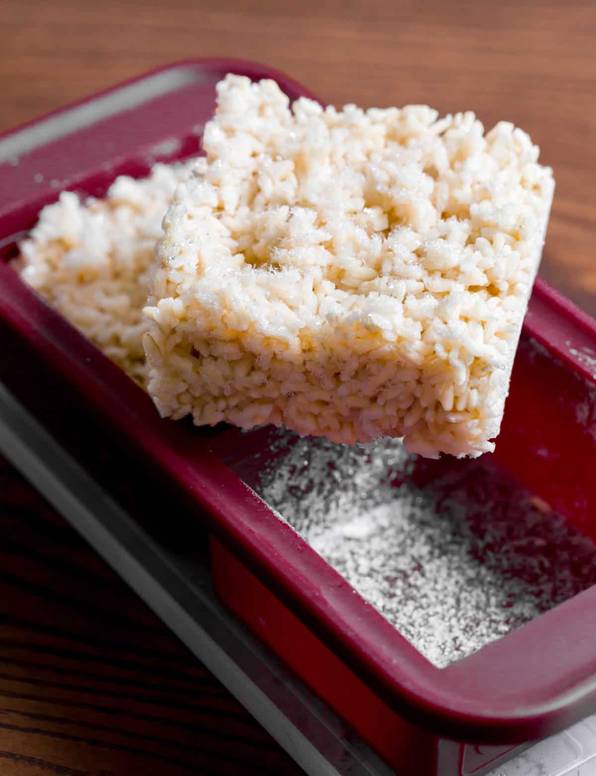 a square block of frozen brown rice sits on top of burgundy silicone souper cube freezer trays