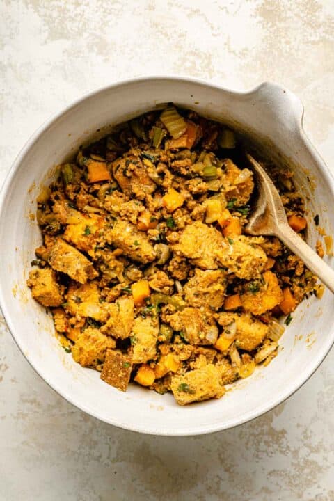 cornbread, sourdough, chorizo, and vegetable mixture in a ceramic bowl with a wooden spoon