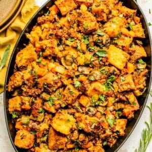 chorizo cornbread stuffing in a black oval cast iron dish next to fresh rosemary and sage