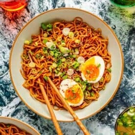 sesame ramen plated in a bowl with wooden chopsticks topped with fresh scallions, jammy eggs, and white sesame seeds.