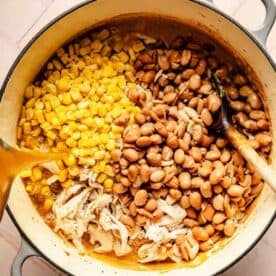 shredded chicken, corn kernels, and pinto beans in a dutch oven with broth being poured over top