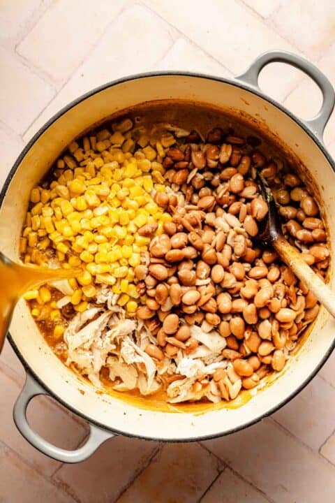 shredded chicken, corn kernels, and pinto beans in a dutch oven with broth being poured over top