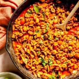 assembled turkey picadillo in a cast iron skillet with a wooden spoon next to a clay colored linen towel